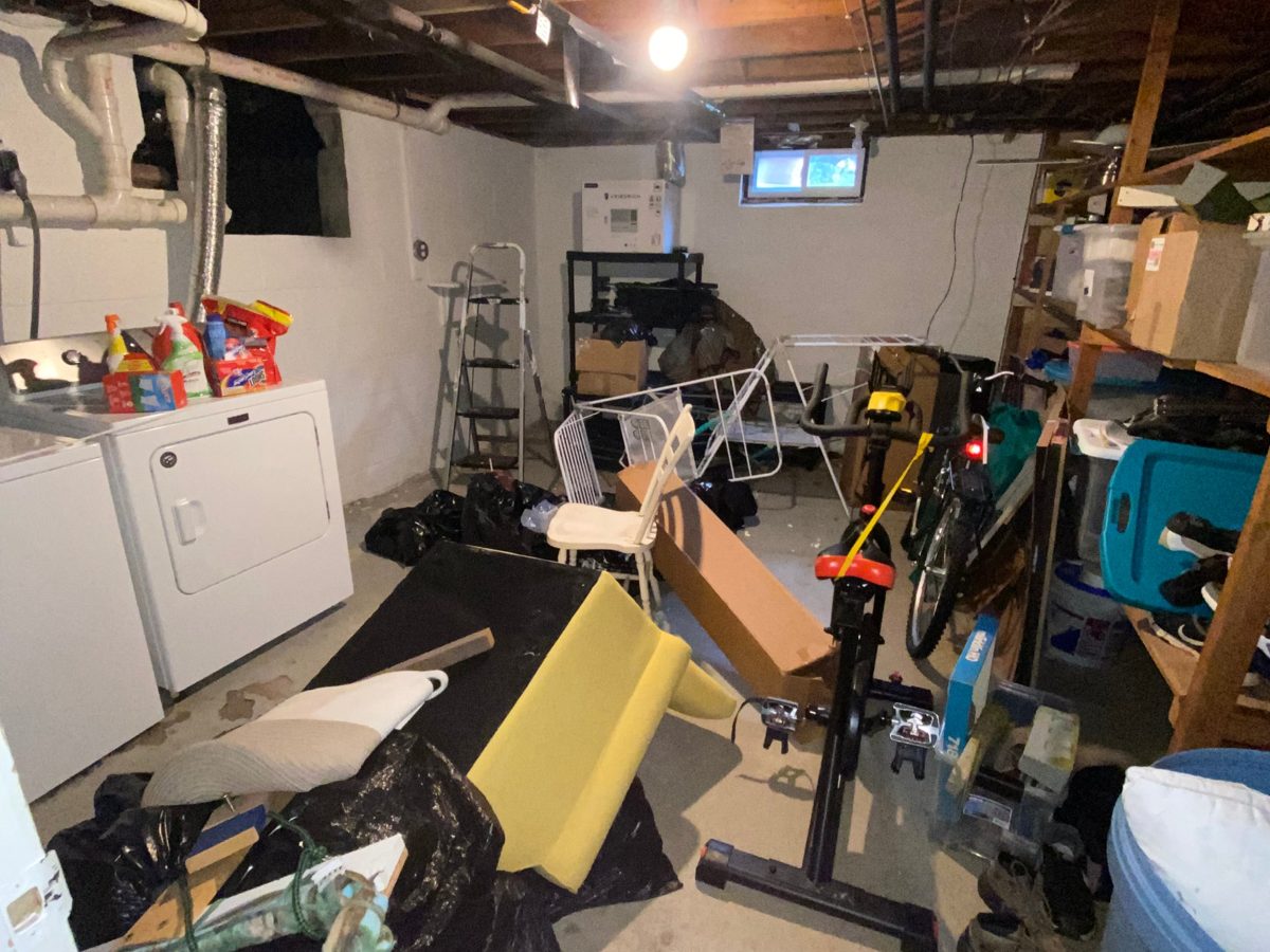 Basement laundry area piled with bags, a bike, furniture, and clutter before a cleanout