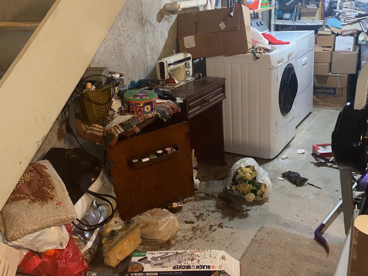 Basement under the stairs filled with bags, furniture, and household items before a cleanout