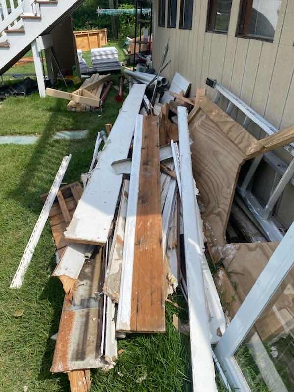 Pile of old siding, boards, and trim beside a house