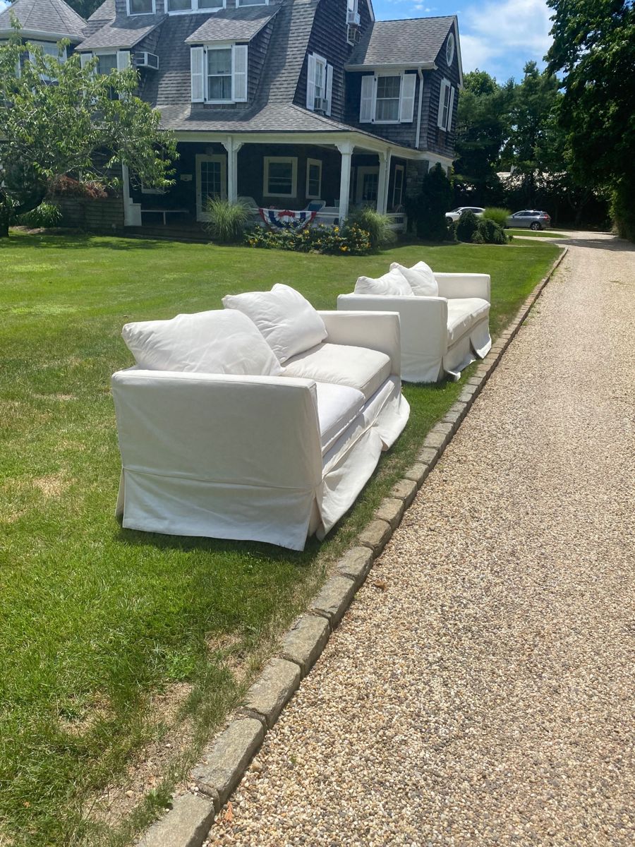 Two white slipcovered sofas set out on a lawn for pickup