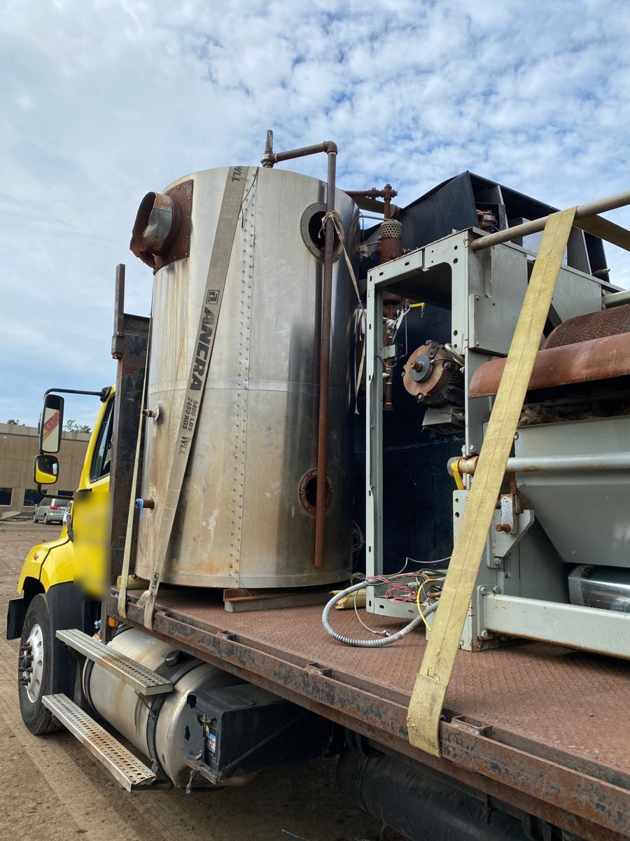Stainless steel tank and industrial machinery strapped down on a flatbed truck