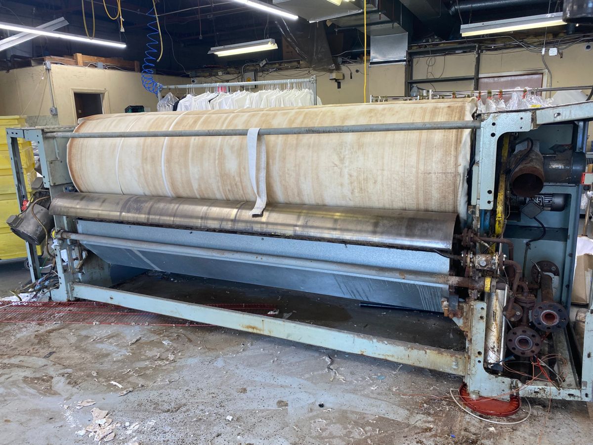 Large industrial laundry ironer with a padded roller inside a commercial plant before removal