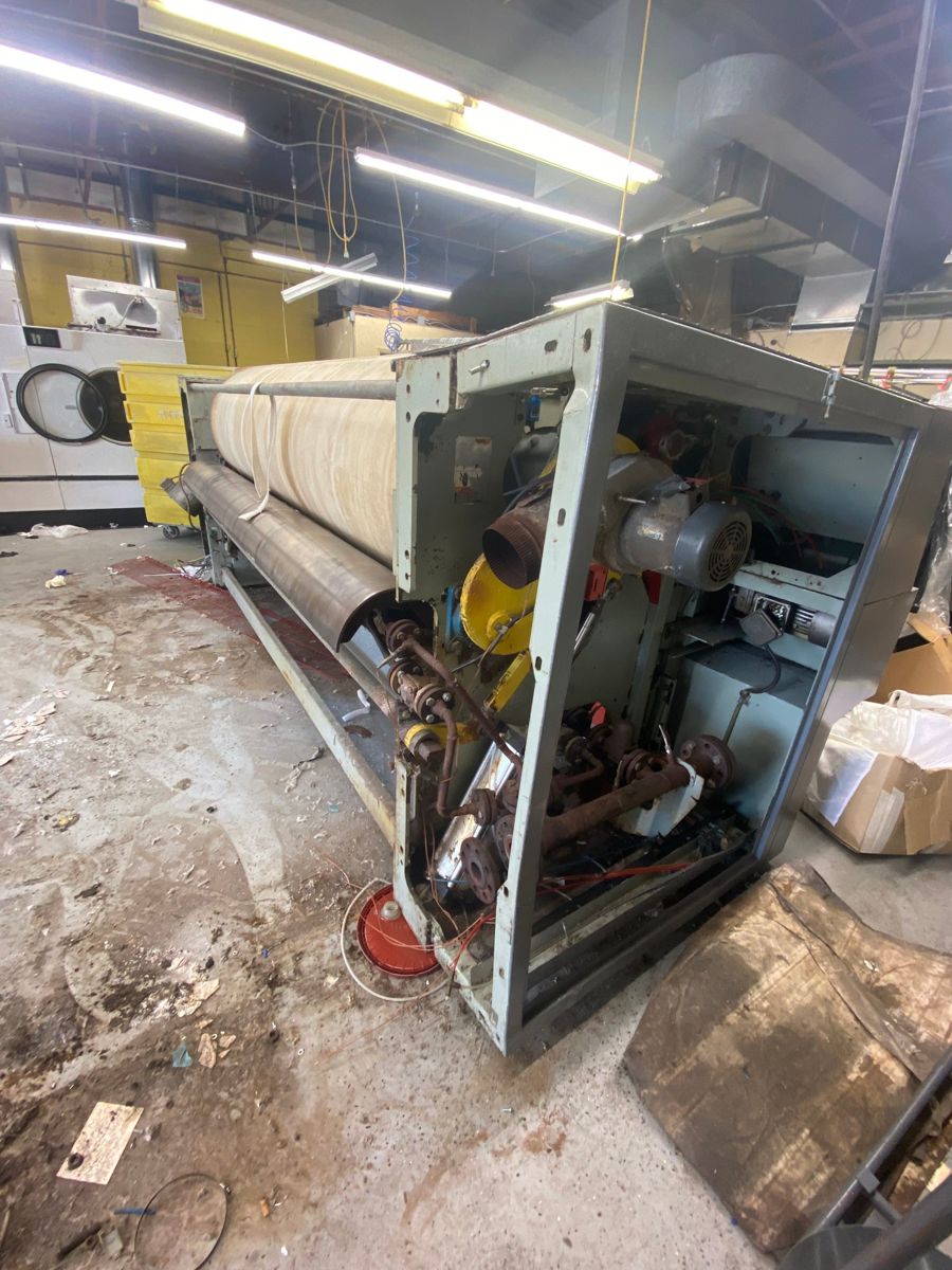 Industrial ironer with its side panel open, showing motors and piping, before removal