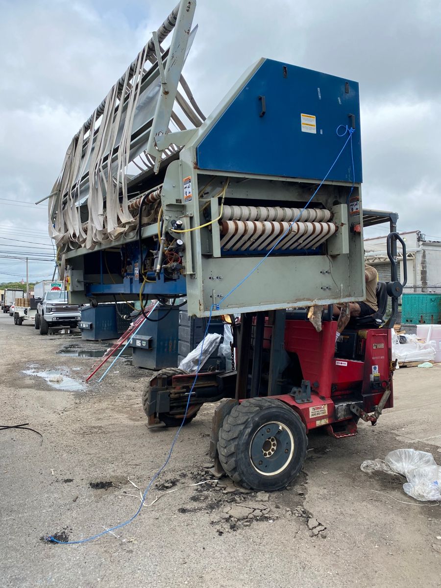 Industrial machine lifted off the ground by a truck-mounted forklift outside a commercial building