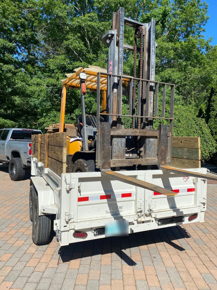 Forklift loaded onto a dump trailer in a driveway