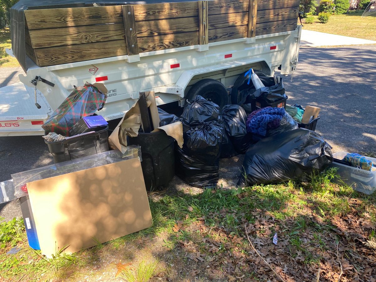 Trash bags, bins, and cardboard piled at the curb beside the dump trailer
