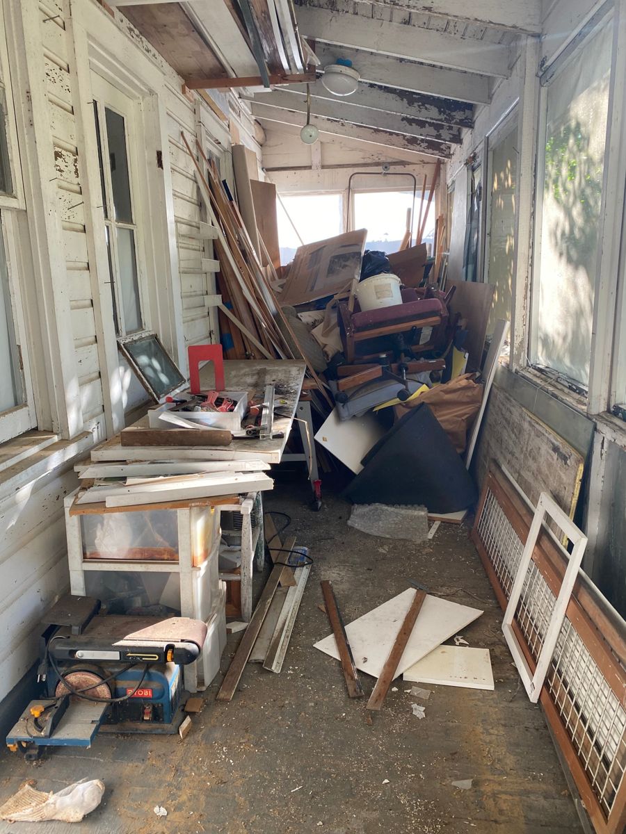 Enclosed porch packed with lumber, furniture, tools, and debris before cleanout