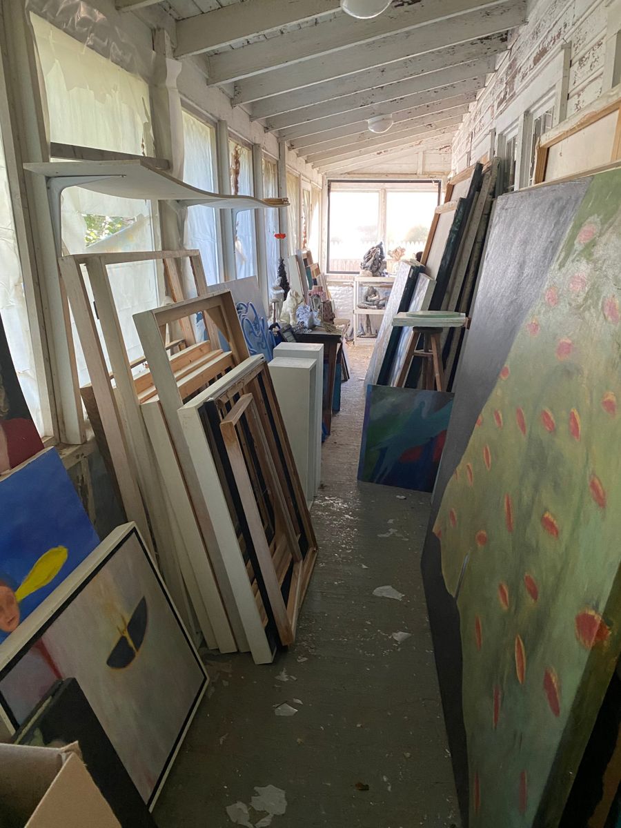 Porch lined with framed canvases, frames, and stored items before cleanout