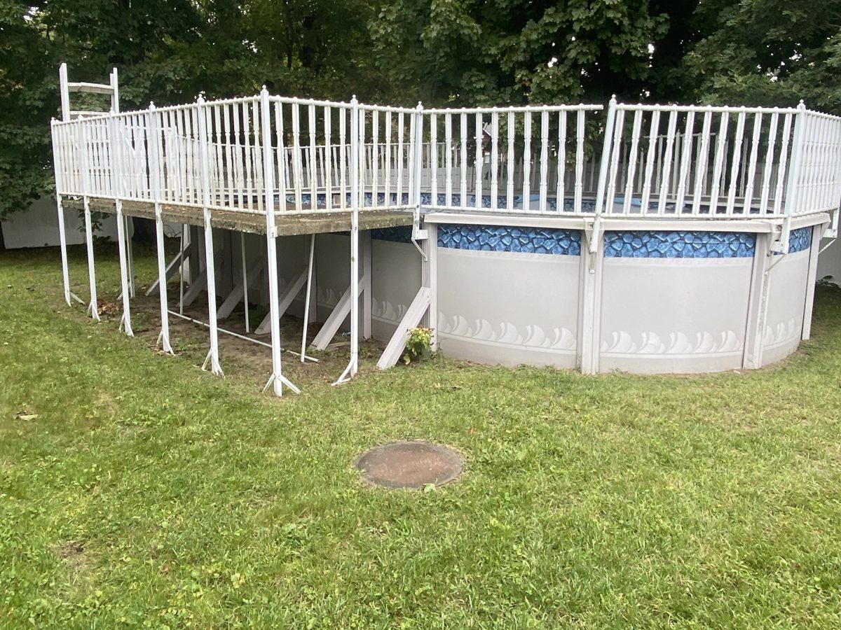 Above-ground pool with a deck and railing in a backyard before removal