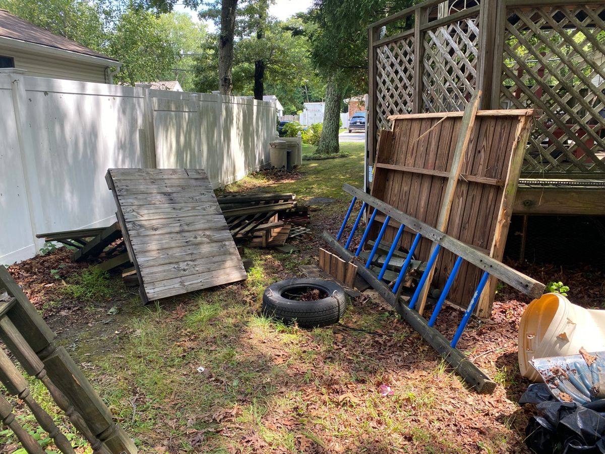 Wood fence panels, a ladder, and a tire piled beside a deck