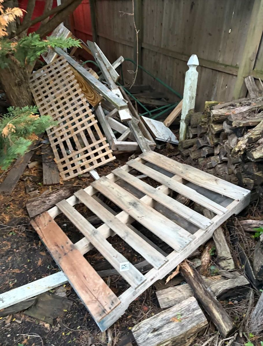 Wood pallets, lattice, and firewood piled in a corner of a yard