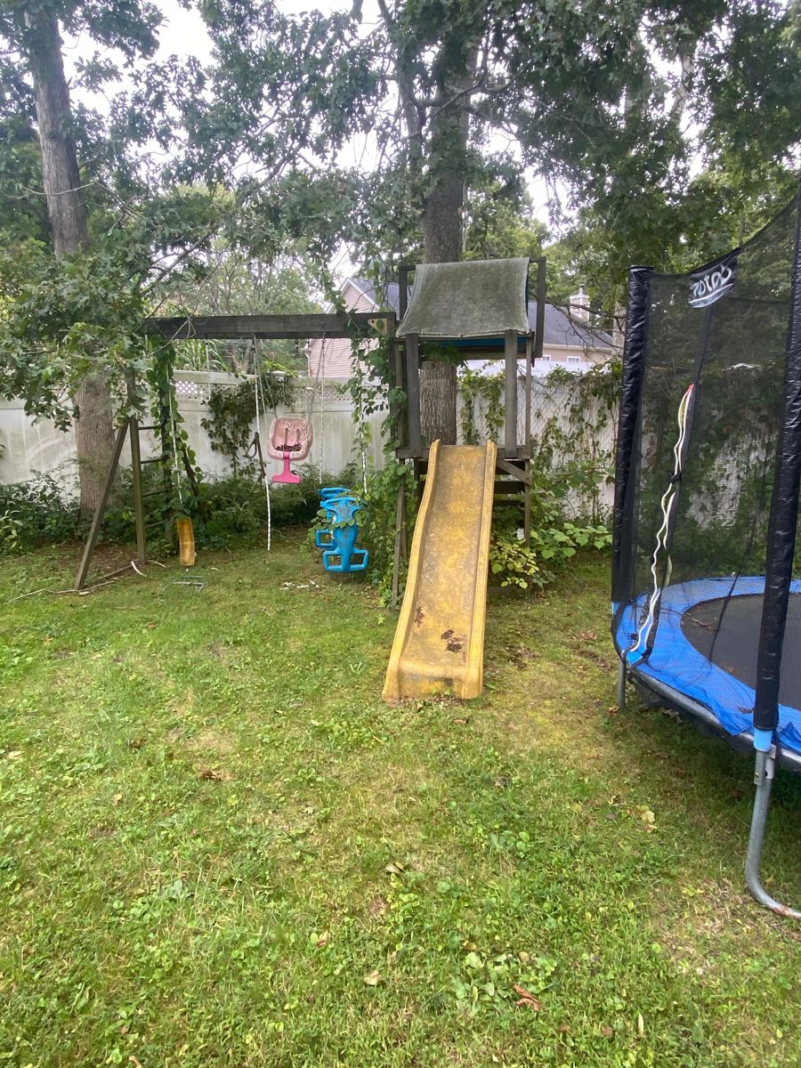 Overgrown backyard swing set and slide next to a trampoline