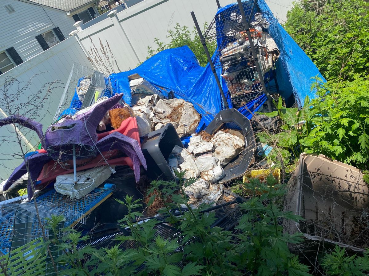 Backyard pile of cages, bins, and debris under a blue tarp