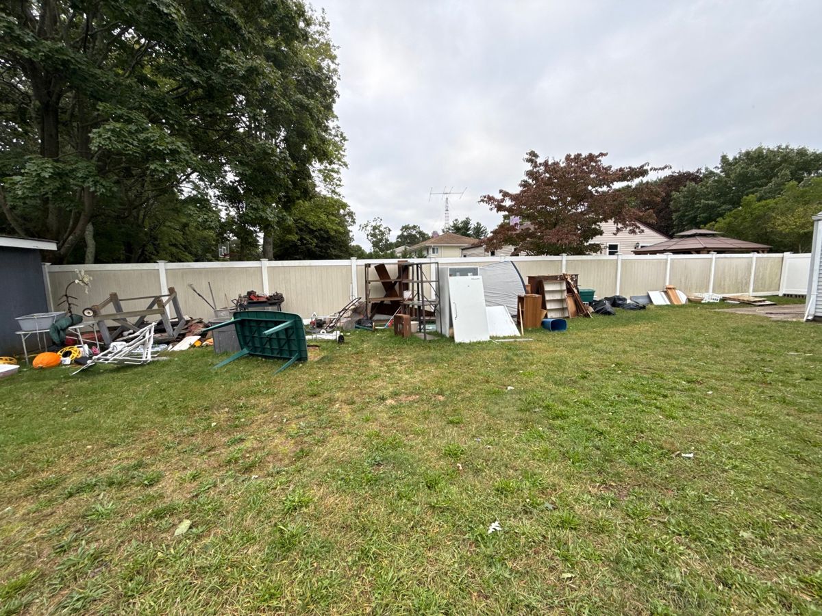 Furniture, shelving, and outdoor items lined up along a backyard fence for removal
